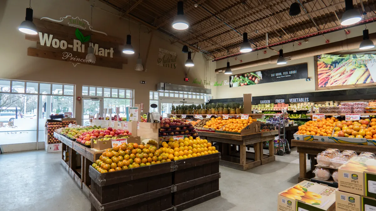 The produce hall at Woo-Ri Mart, with the store sign above the fruit tables and daylight from the front windows